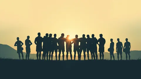 Illustration of silhouetted teammates joining hands in a huddle at sunset